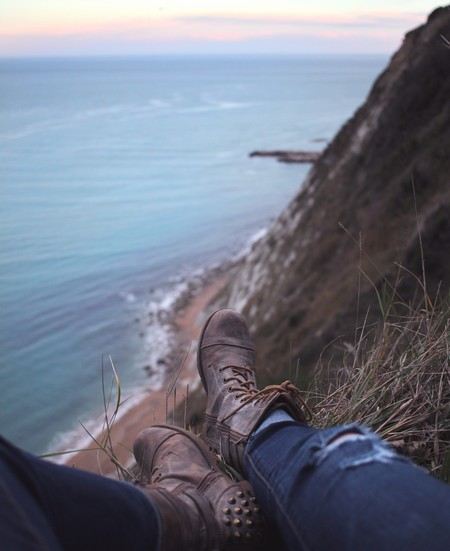 só se vêm os jeans e botas de alguém sentado a pique sobre uma falésia que dá sobre o mar